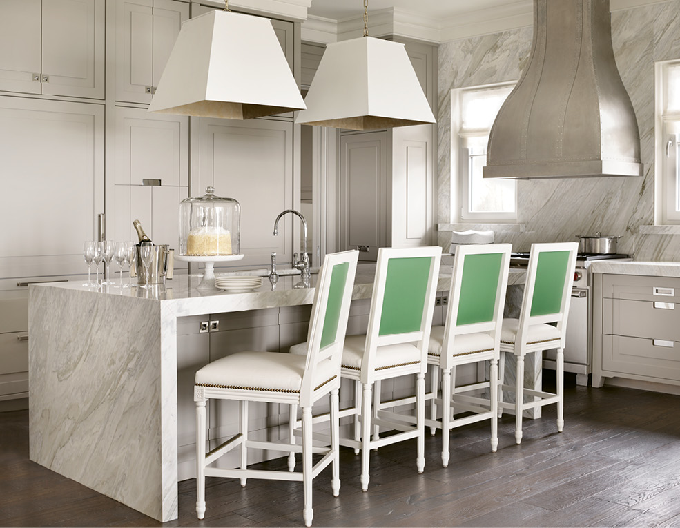 The kitchen sets a luxe tone with its walls and waterfall island wrapped in Calacatta Gold Extra marble as well as brass-lined light fixtures by Avrett, while custom chairs outfitted with white vinyl and green leather add graphic punch.