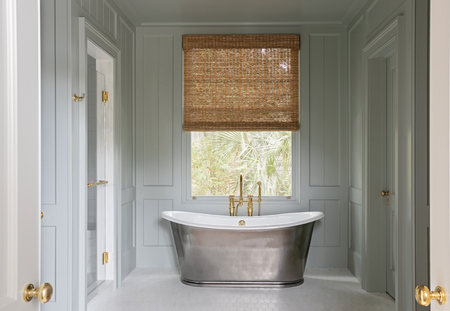 A freestanding cast iron tub from Waterworks with brass fixtures from Bird Hardware is a centerpiece in the panelled room painted in Farrow &amp; Ball “Light Blue.”