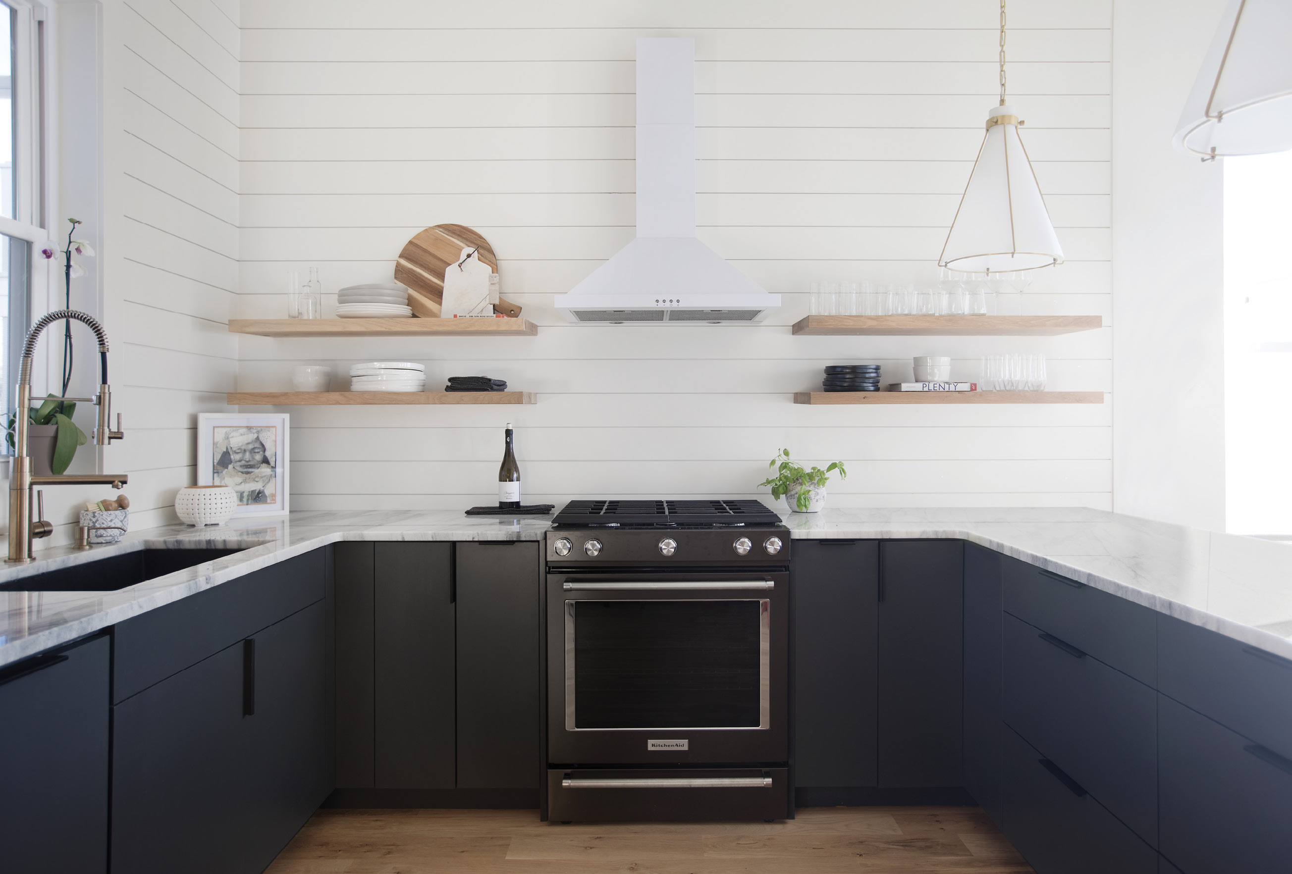 LINEAR THINKING: Open shelving and shiplap walls create an inviting kitchen space that flows seamlessly from the adjoining dining area, replete with green velvet chairs by Moes (“They’re so easy to clean!” says Vickers). She chose shiplap as it’s less expensive than a tile backsplash and helped with the continuity of the space.