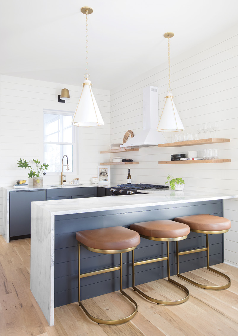 LUXE DETAILS: Rio Venato marble countertops that waterfall to white oak flooring provide a high-end focal point, contrasting beautifully with the dark cabinetry and Alder and Tweed leather and bronze stools. A pair of Hudson Valley pendant lights complete the modern, organic look.