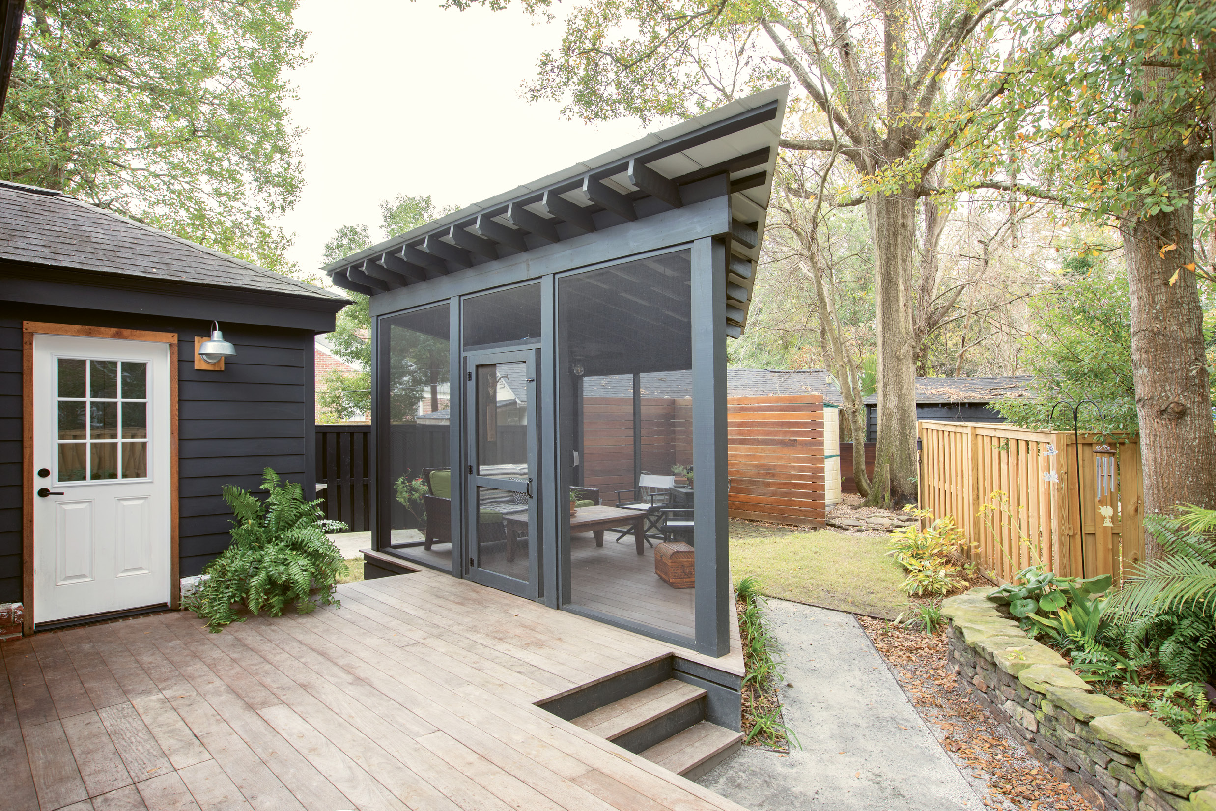 PRIME PERCH: Just off the back deck, an angular screened-in porch makes the most of the triangular lot; its tin roof adds an industrial touch that feels perfectly in step with the rest of the modern-minded renovation. “I’m so glad we made the screened-in porch happen: I love being outside, but the no-seeums drive me nuts,” Jacques says. “There’s nothing better than sitting on the couch outside, listening to the wind blow, birds sing, and children playing in the neighborhood.”