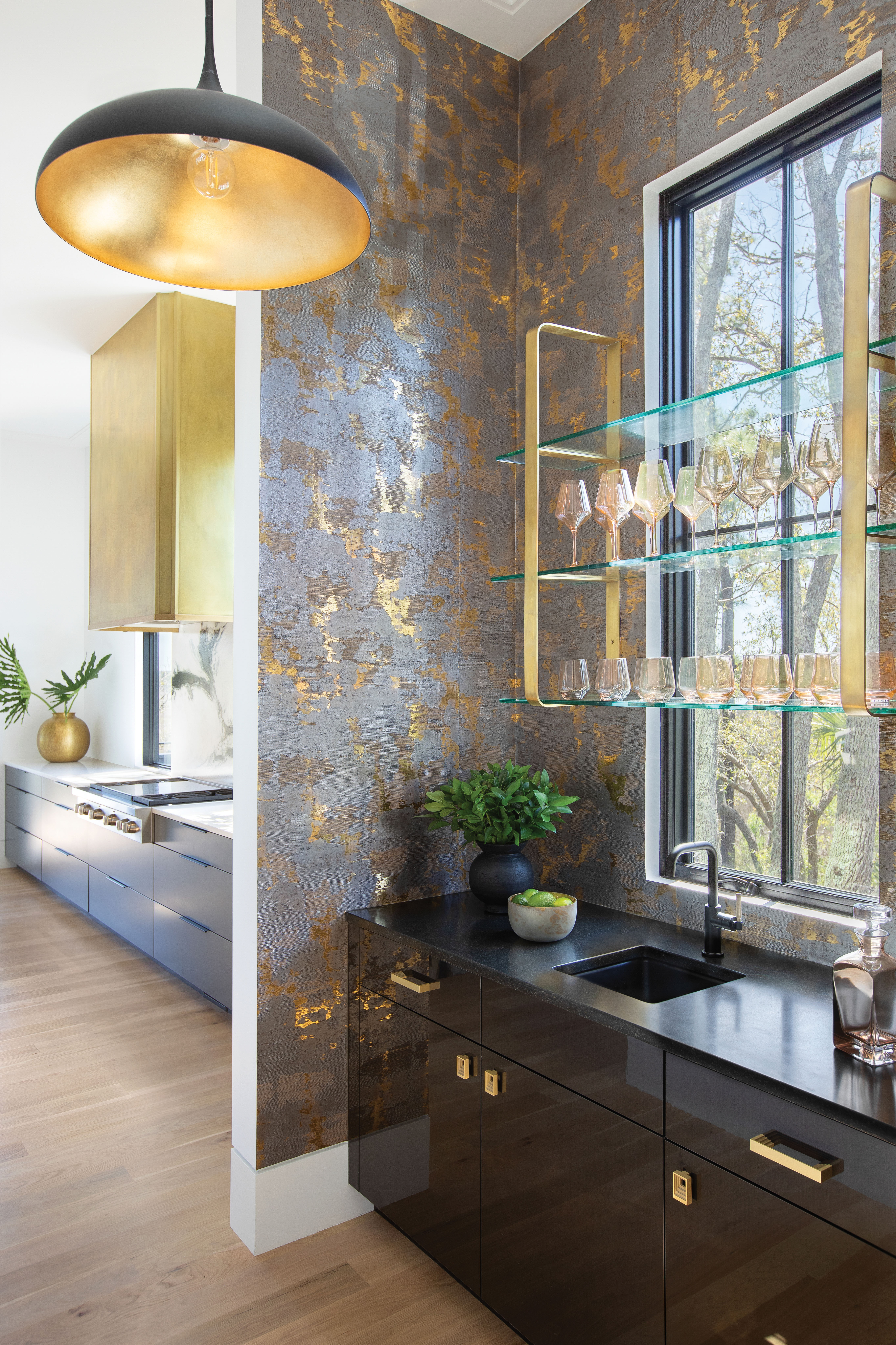 Brass Tactics: In the adjoining wet bar, Phillip Jeffries metallic “Enlightenment” wallpaper in “Tantra Taupe” complements a handcrafted set of floating brass and glass shelves by Bryan Reiss.