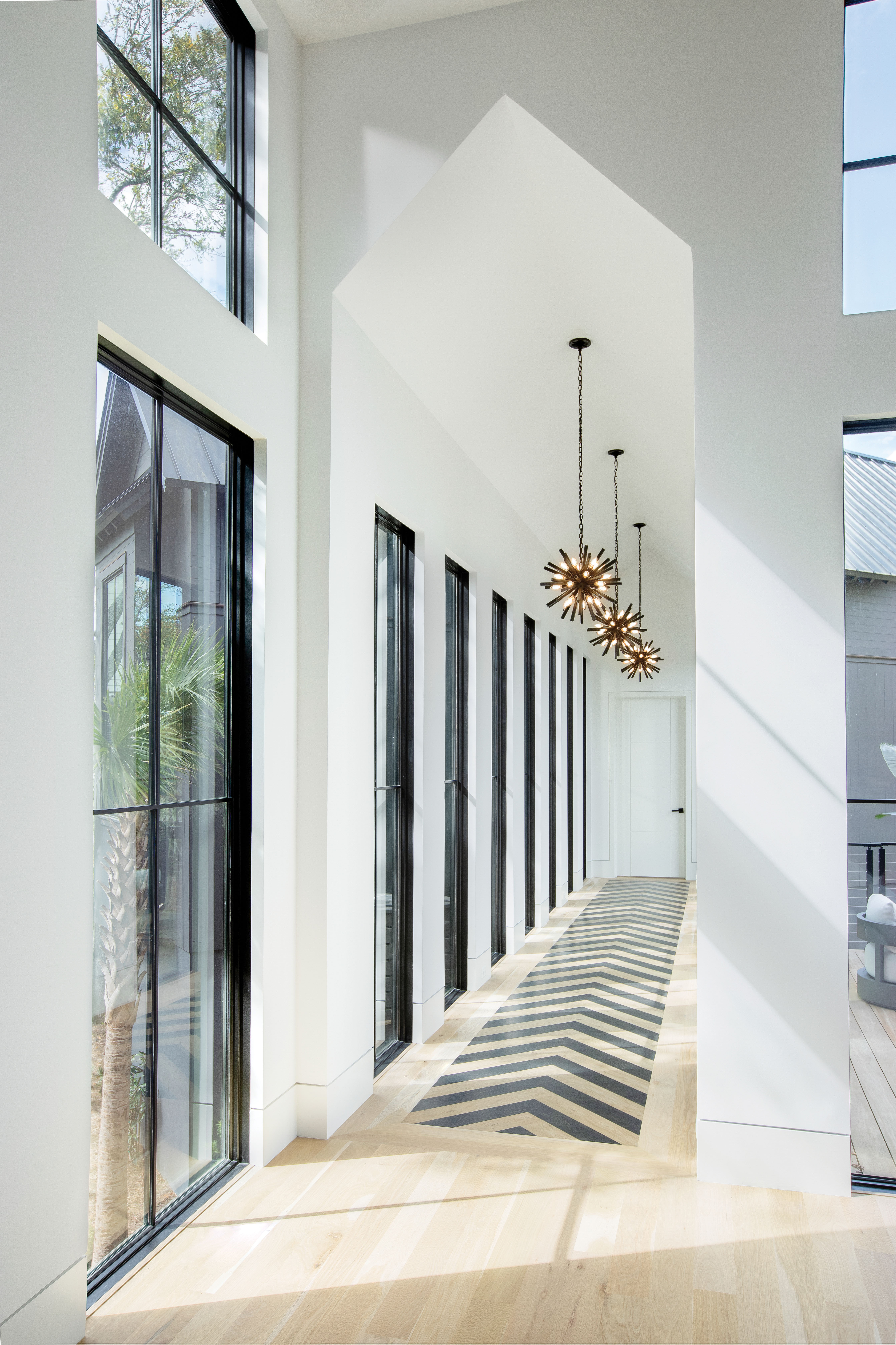A long, window-filled corridor leads from the main living space to the homeowners’ bedroom suite.