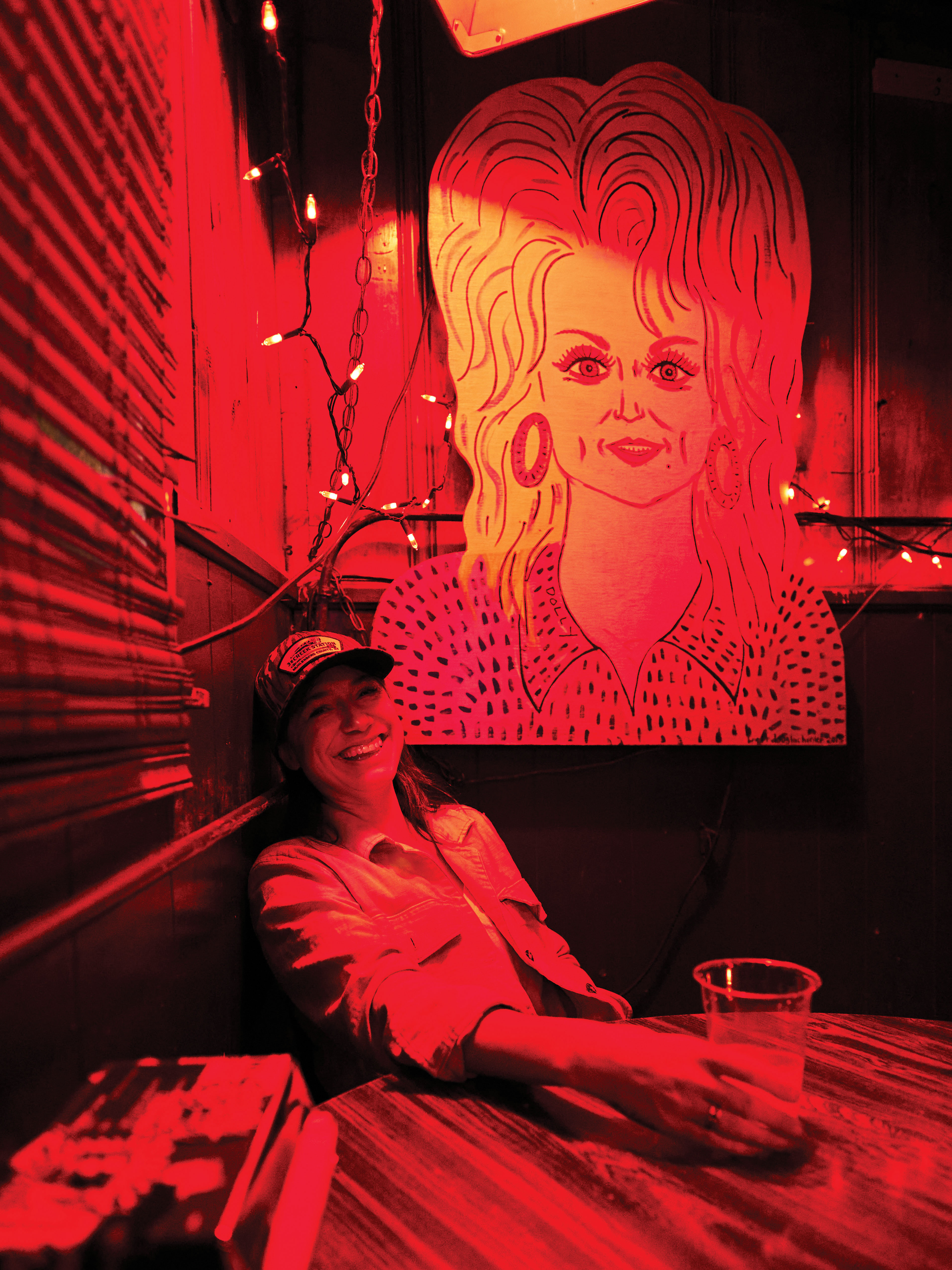 Musician Arum Rae under one of the Dolly Parton portraits at Dino’s, a dive bar in East Nashville.