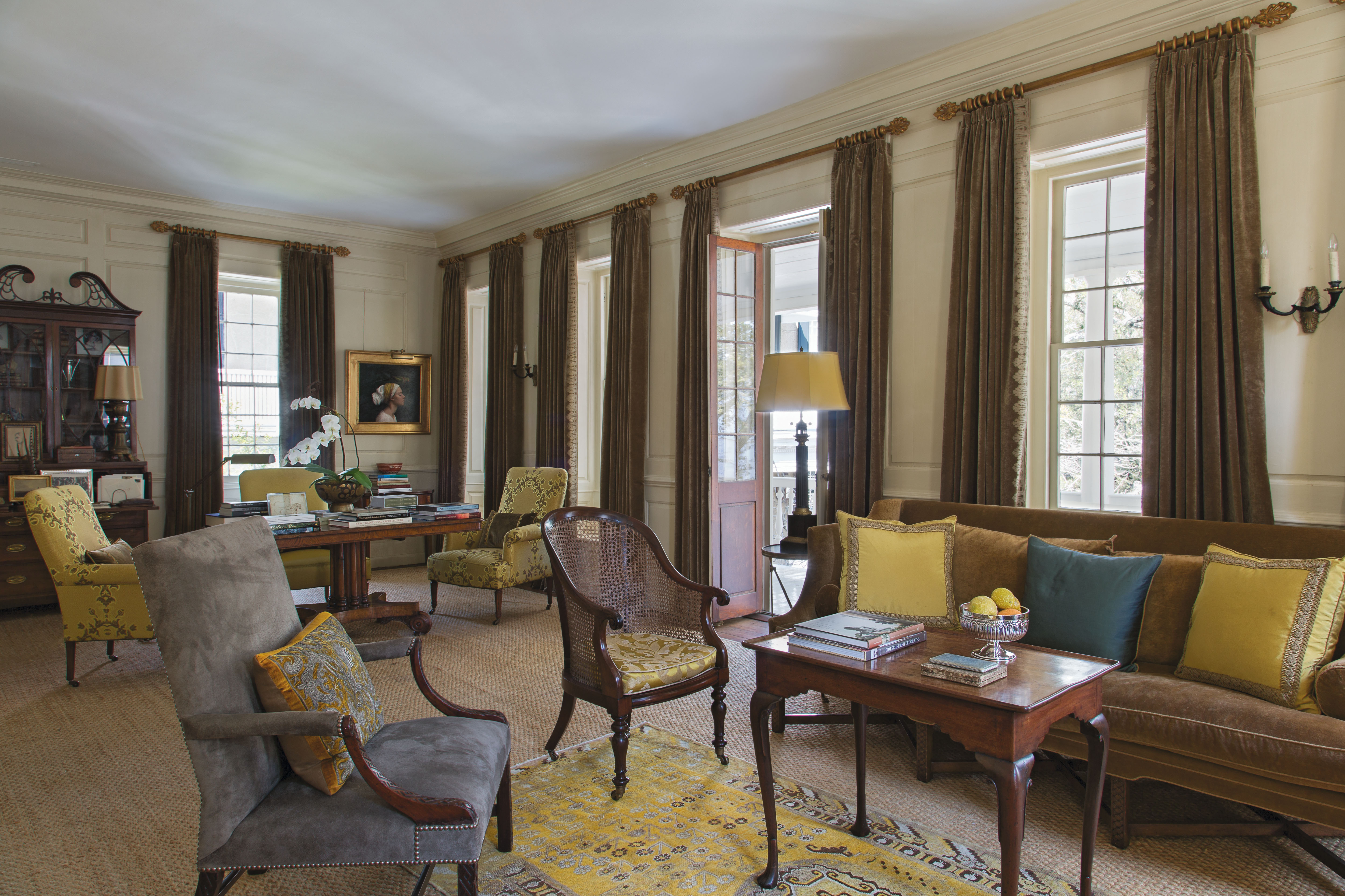 The upstairs drawing room is outfitted in a sophisticated palette of rich browns and yellows. An inviting mix of textures, from an antique Khotan rug atop seagrass to suede upholstery on the 18th-century armchair, adds visual interest, as do works by Ben Long and Louise Fenne.