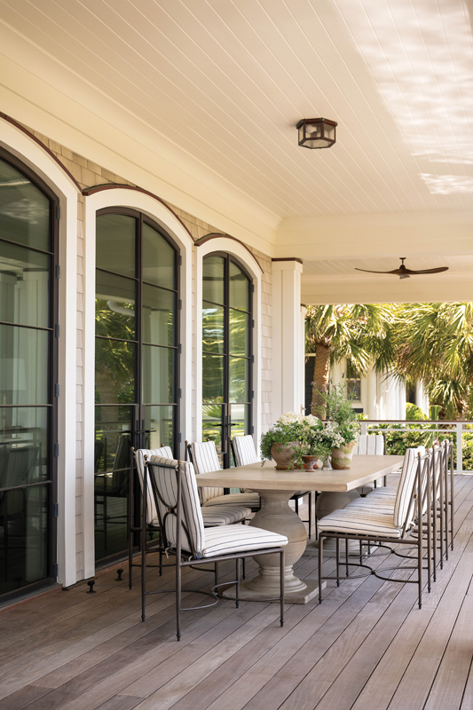 Expansive porches combine Lowcountry and New England architecture to create generous spaces for gathering and taking in the ocean views. A Made Goods table and Summer Classics chairs offer an opportunity for alfresco dining just outside the main living space.