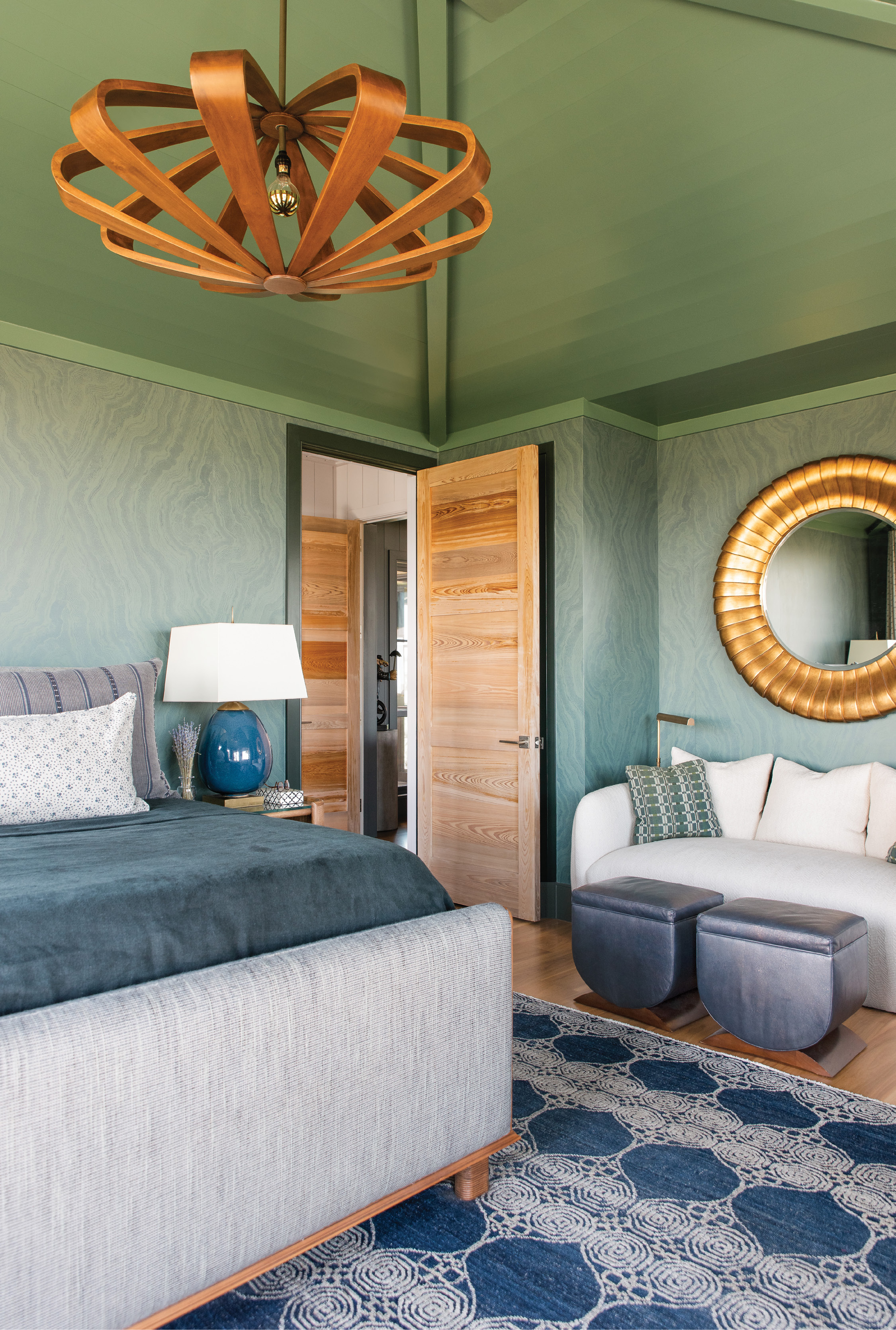 Into the Deep: A wood ceiling painted in a custom green hue encapsulates this cozy master bedroom, replete in deep blues that mimic the ocean beyond. A sunken cypress door and the “Remus” saucer pendant light by Arteriors contrast with the wallpaper, designed by Apparatus in collaboration with ZAK+FOX, that provides a soothing backdrop for a peaceful night’s rest.