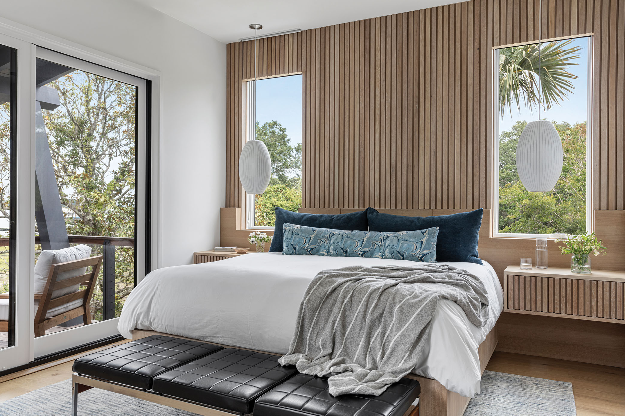 The headboard and side tables are integrated with the walls and windows, adding function and form. Two Nelson “Cigar Bubble” pendant lights and a vintage leather bench bring a touch of style to the simplicity.