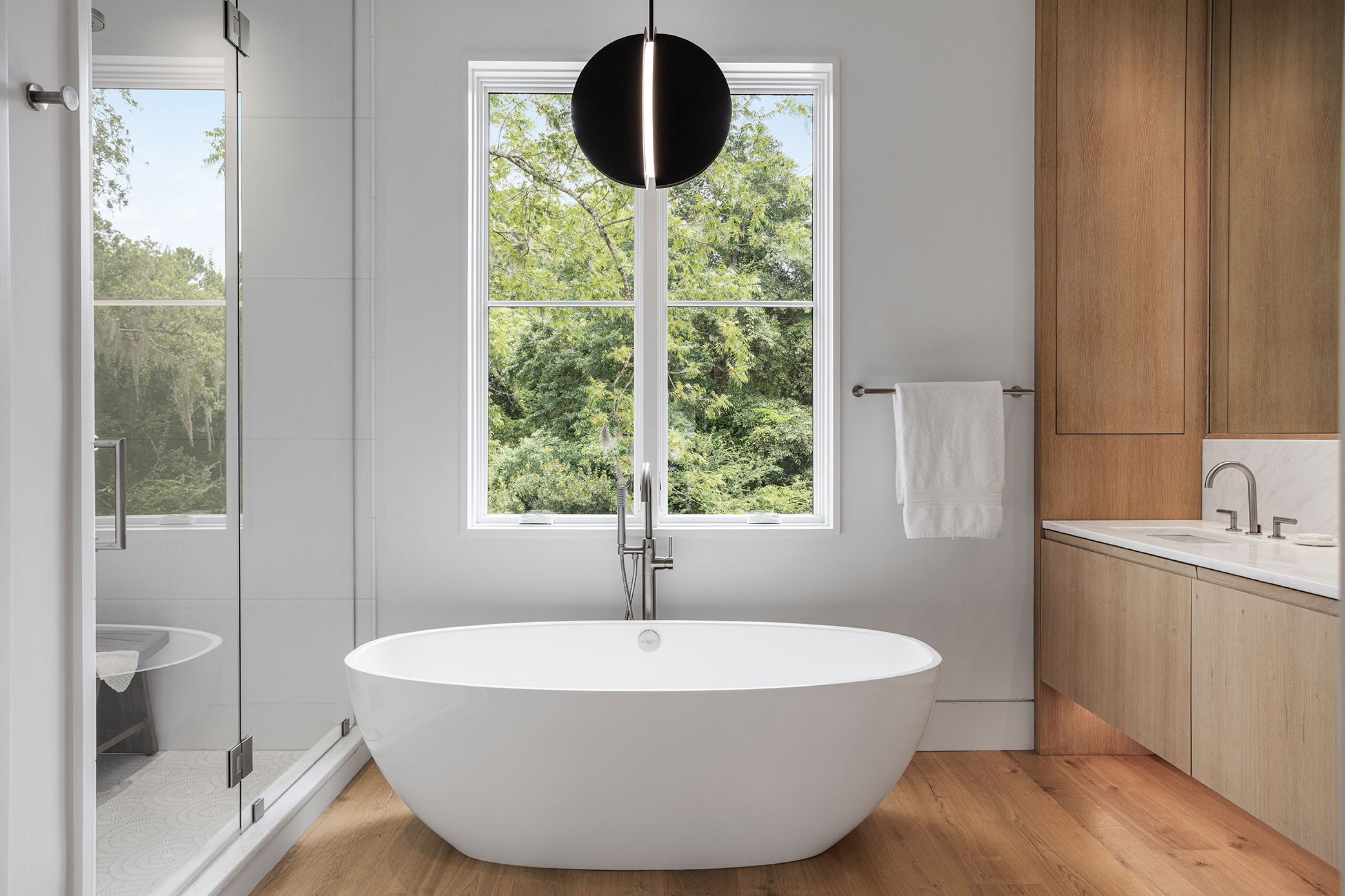 In the adjoining bath, a soaker tub is topped by a black pendant light from Visual Comfort.