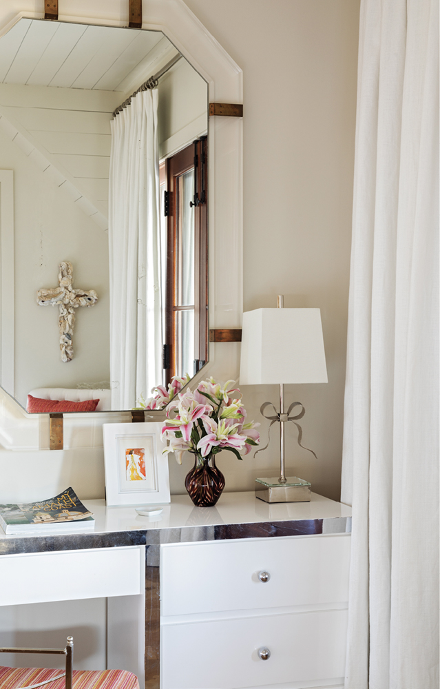 In a guest bath, a pair of chrome ribbon lamps sit atop a vintage dressing table with a Lucite and brass mirror.