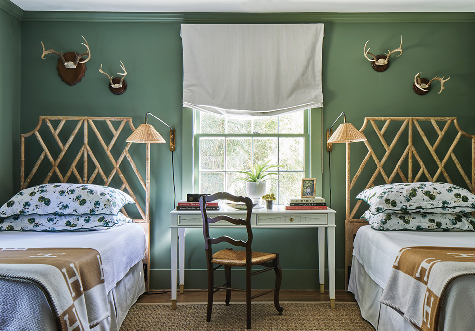 This guest room speaks toward nature, with mounted antlers, bamboo headboards, and sage green walls (Farrow &amp; Ball’s “Calke Green”). “We upgraded the standard pillows to king size, which makes sleeping solo in a twin bed the biggest treat,” says the designer.