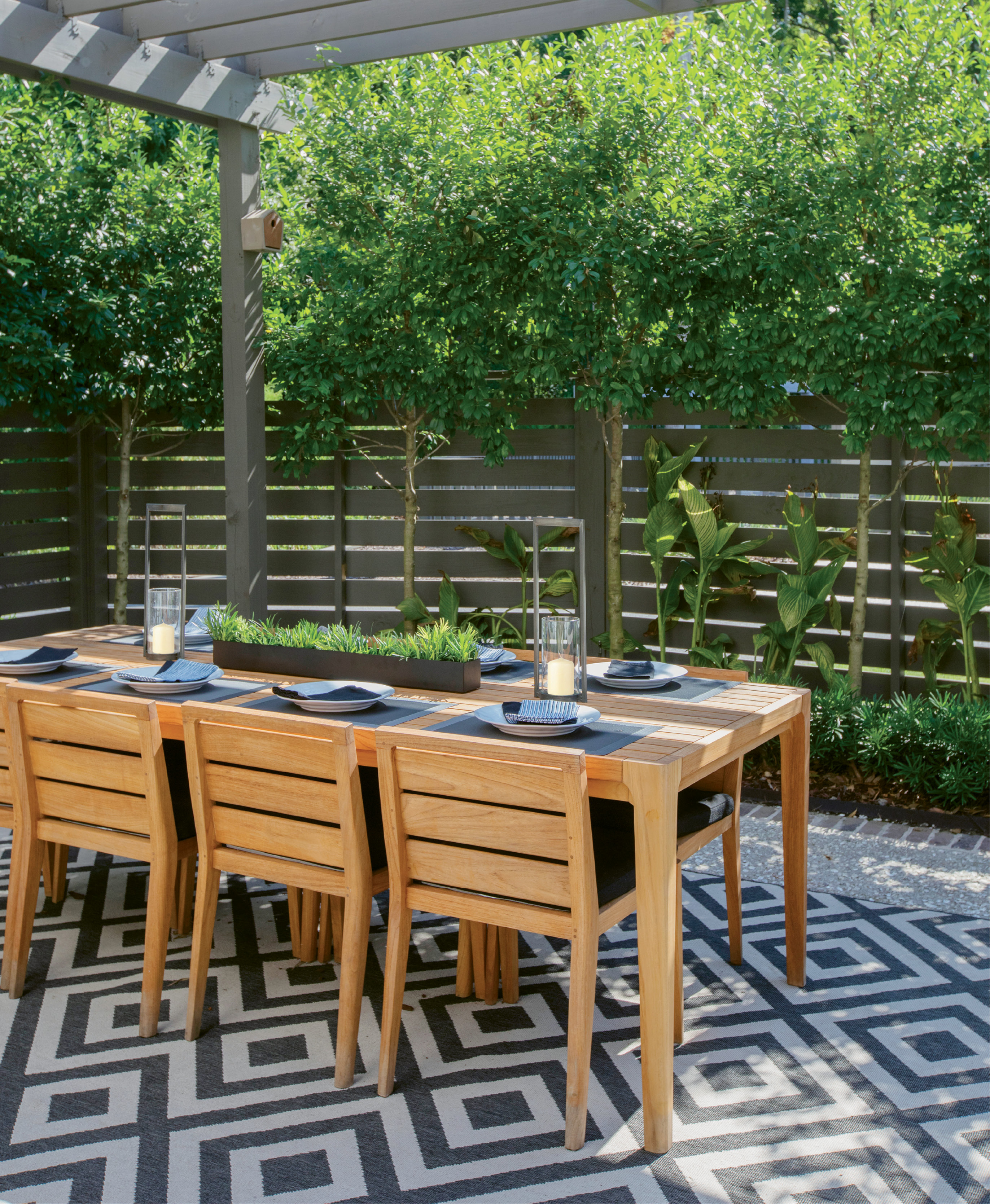Limbed holly bushes soften a horizontal wood-slat fence, providing privacy as well as filtered light for the Thomae family’s alfresco dining room.