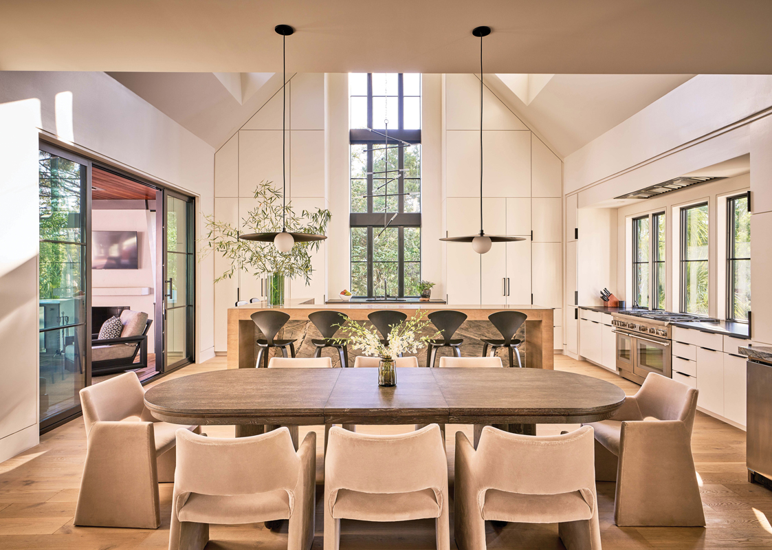 Crave-Worthy: The kitchen/dining space is dominated by a cabinet wall that extends to the 20-foot-high ceiling. A modern wood and stone island lit by custom fixtures from Fourteenth Colony serves as a gathering spot. White velvet Norman Cherner chairs surround a Codarus oak table, providing contrast with the black accents in the kitchen.