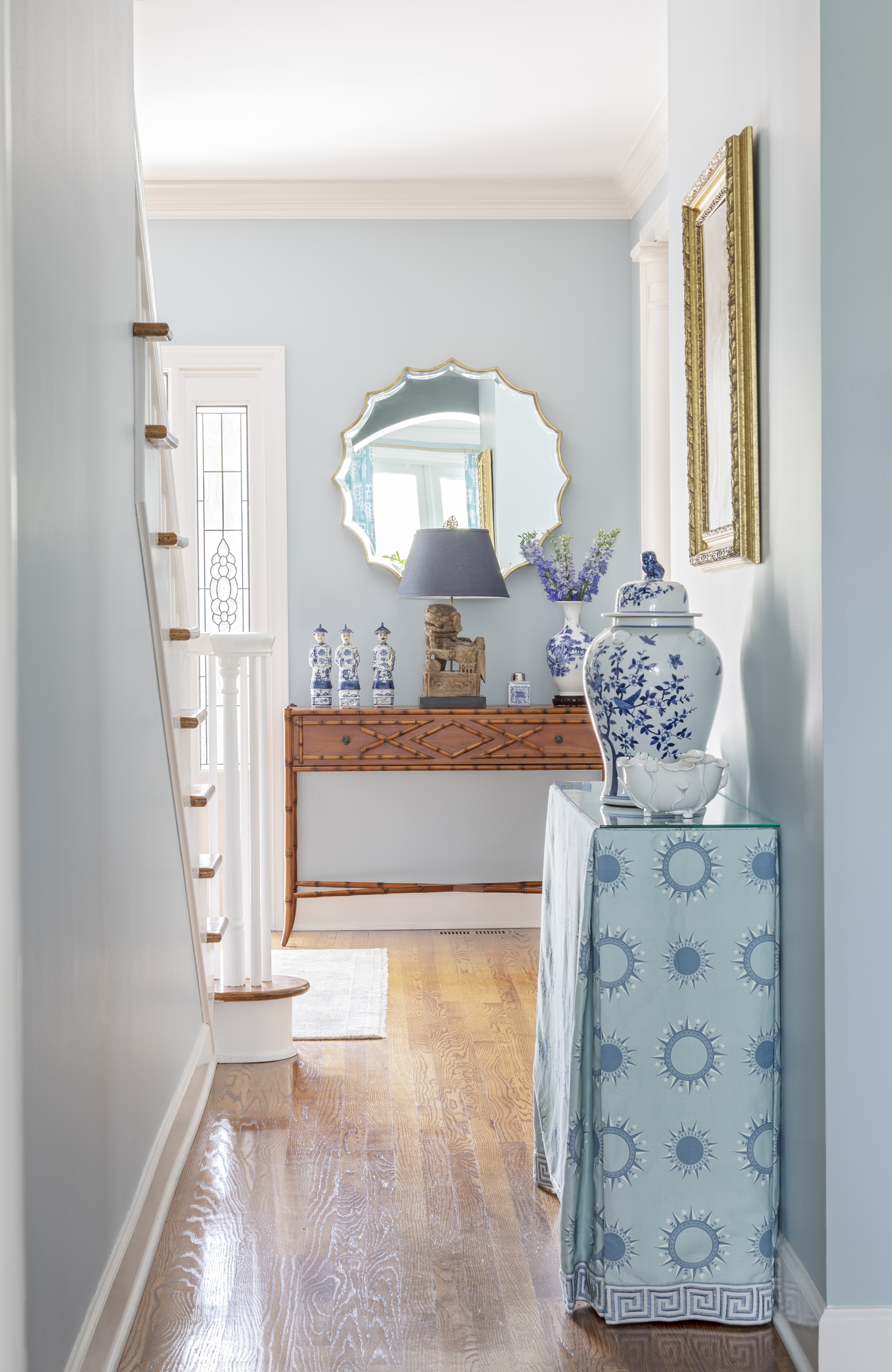 MIRROR MIRROR: A pair of matching console tables, skirted in fabric designed by Horton, display antique ginger jars from Well Furnished in the entry hall, where an aged brass mirror from Ballard Designs reflects the light from the marsh front windows to brighten the otherwise dark space.
