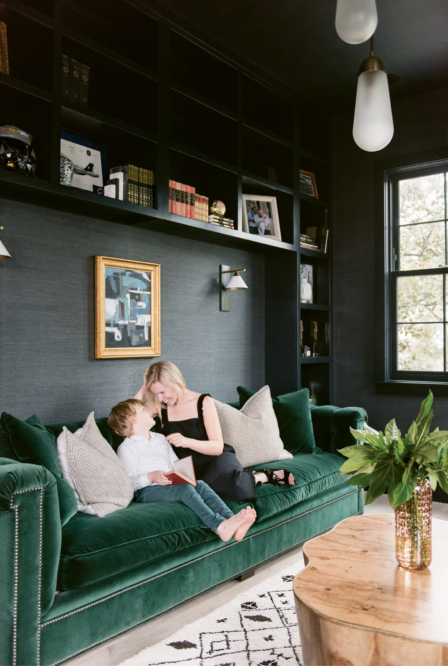 Molly and Sawyer read in the library, where the Phillip Jeffries “Manila Hemp” wallpaper in “charcoal” and Hickory Chair sofa upholstered in emerald-green velvet by Ralph Lauren set a moody, masculine tone.