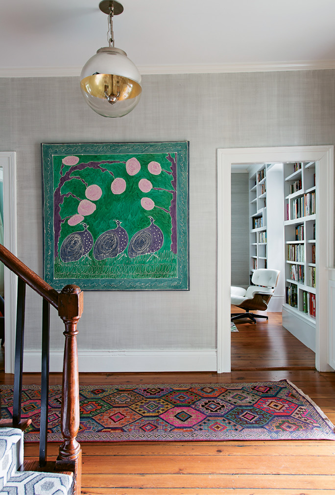 BOLD ACCENTS: Grasscloth wallpaper provides a neutral backdrop for the foyer’s bright silk painting and two patterned rugs.