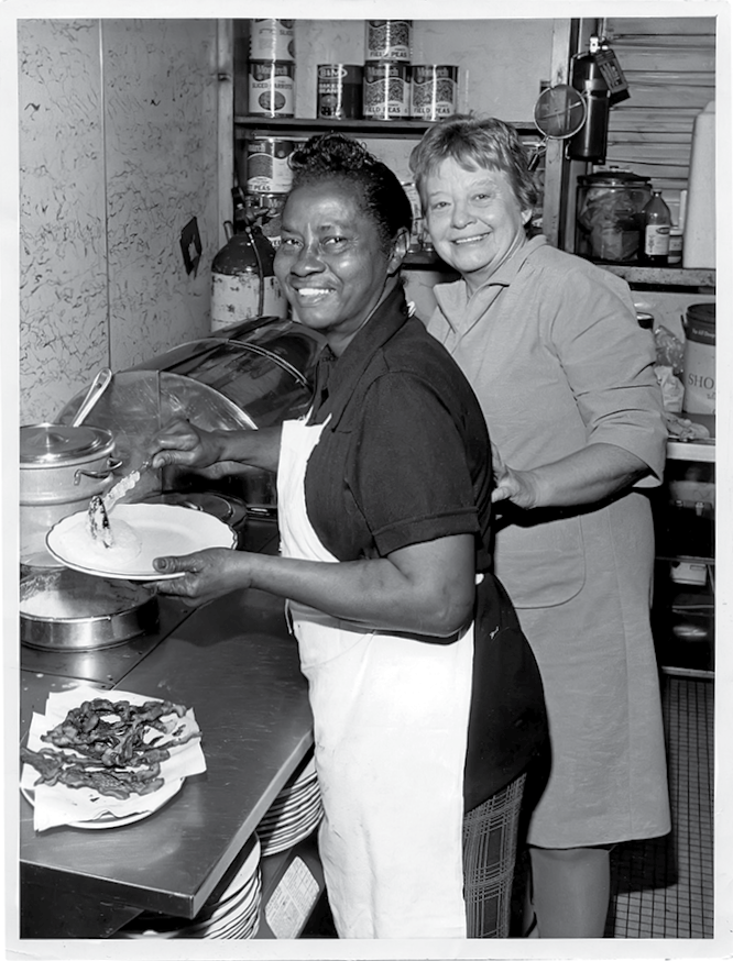 Miss Kitty Proctor dishing up Southern eats with a smile in the 1970s alongside Maddie Heneghen