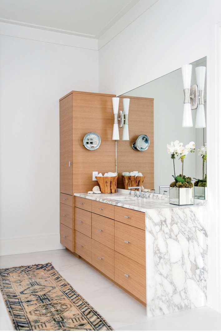 White oak cabinetry and a vintage runner warm the marble-clad master bath. The sconces are from Circa Lighting.
