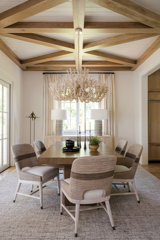 Natural Origins: Wood detailing on the ceiling helps delineate the dining room from the kitchen and living room. Hand-twisted lampakanai rope chairs and a large oak table from Palecek top a wool rug, adding organic interest to the clean space. A showpiece “Seychelles Coco” chandelier from Palecek, with its coral-inspired look, hints at the coastal setting.