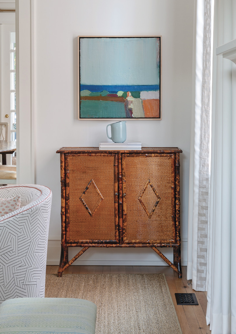 NEUTRAL TERRITORY: Benjamin Moore’s ‘Simply White’ is the backdrop for a mix of natural hues throughout the home, from white oak flooring to a Fibreworks rug, allowing certain pieces to pop, such as this bamboo cabinet from Acquisitions and Sandy Ostrau abstract oil painting from Meyer Vogl Gallery.