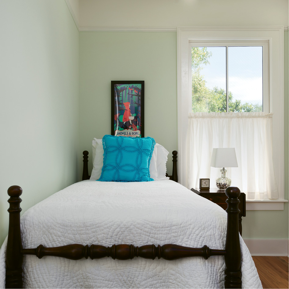 In this petite guest room, a vintage twin bed with a carved pineapple motif and a Shovels &amp; Rope poster add local flavor.