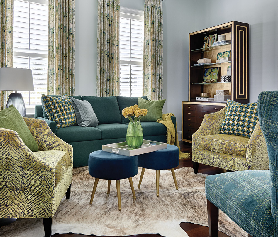 Two Baker “Butterfield Barrel Chairs” covered in a citrus-green fabric provide the focal point for the striking home office. Peacock feather drapes, a cowhide rug, and two velvet footstools complete the luxe look.