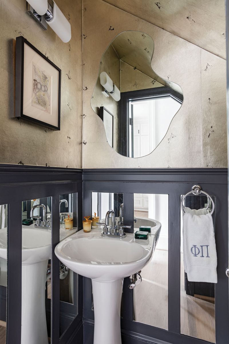A powder room tucked underneath the staircase features a Salvador Dali sketch, skillfully surrounded by mirrors and metallic wallpaper.