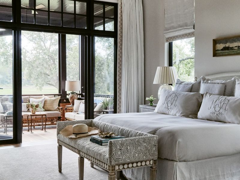 SERENE SCENE: The master suite is a haven of serenity—from the freestanding soaking tub with views of the trees to a quaint and comfortable screened porch, perfect for lounging with coffee. Custom pillows brighten the space, including two wrapped in a brightly colored Clarence House fabric and lumbar varieties in Lucas’s own line, House of Harris. Vintage-inspired pieces, such as the Henredon “Arianna” bench in Mokum fabric, create a feeling of timelessness