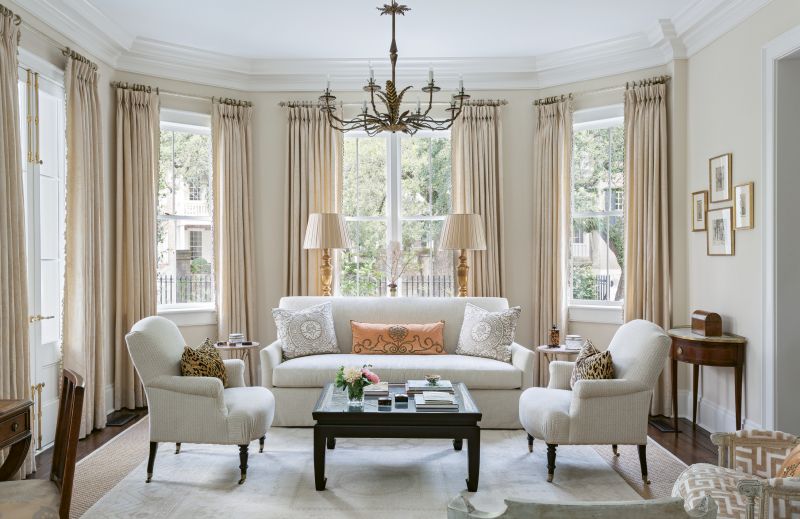 QUIET ELEGANCE: Cream walls with cream damask curtains and neutral upholstery create a timeless background in this large living room. Pillows of leopard velvet, Fortuny damask, and melon velvet with vintage trim add texture and color, while Spanish Barcelona gilt tole chandeliers from David Skinner Antiques provide playful whimsy.