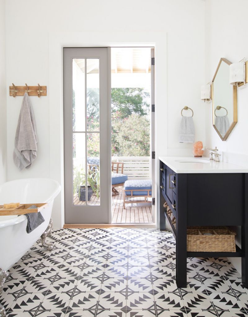 The adjoining bath features the same tile as the kitchen backsplash, custom vanities by cabinetmaker David Beason, a clawfoot tub from Moluf’s, and two “Drake” hemp-wrapped brass wall sconces from Ro Sham Beaux. Both rooms open to a private porch outfitted with cushioned teak chaise lounges and chairs from Tommy Bahama.