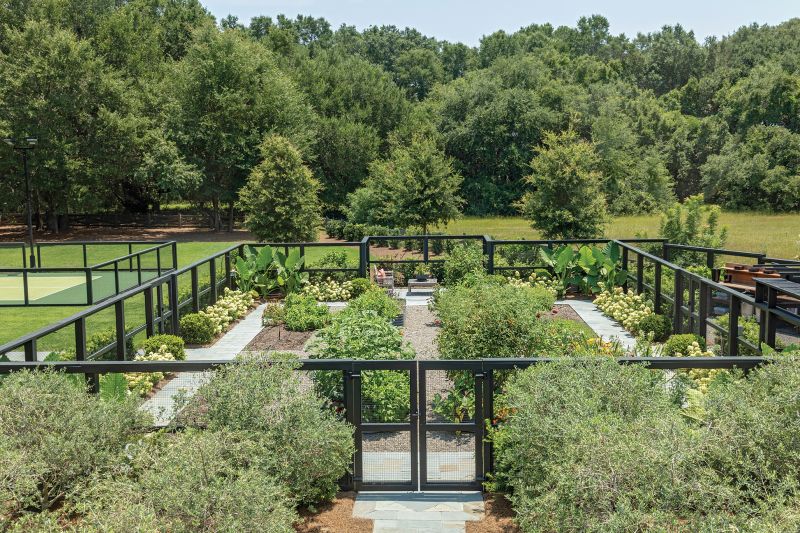 A large flower and vegetable garden and chicken coop adjoin a pickleball court. Along with the pool deck, pathways, and driveway, the court is made from permeable materials to optimize water drainage across the property.