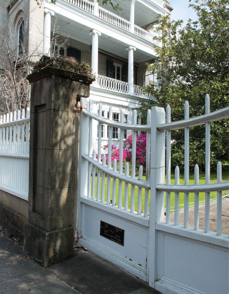 A white picket gate complements the wooden railings and columns of a neoclassical porch.