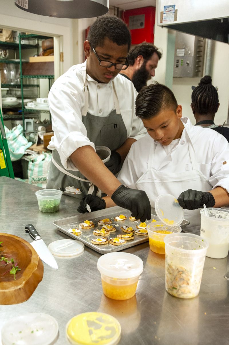 Former Little Chef and current Halls Signature Events intern Aiden LaFave helps Little Chef Abraham Aguilera put finishing touches on bruschetta.