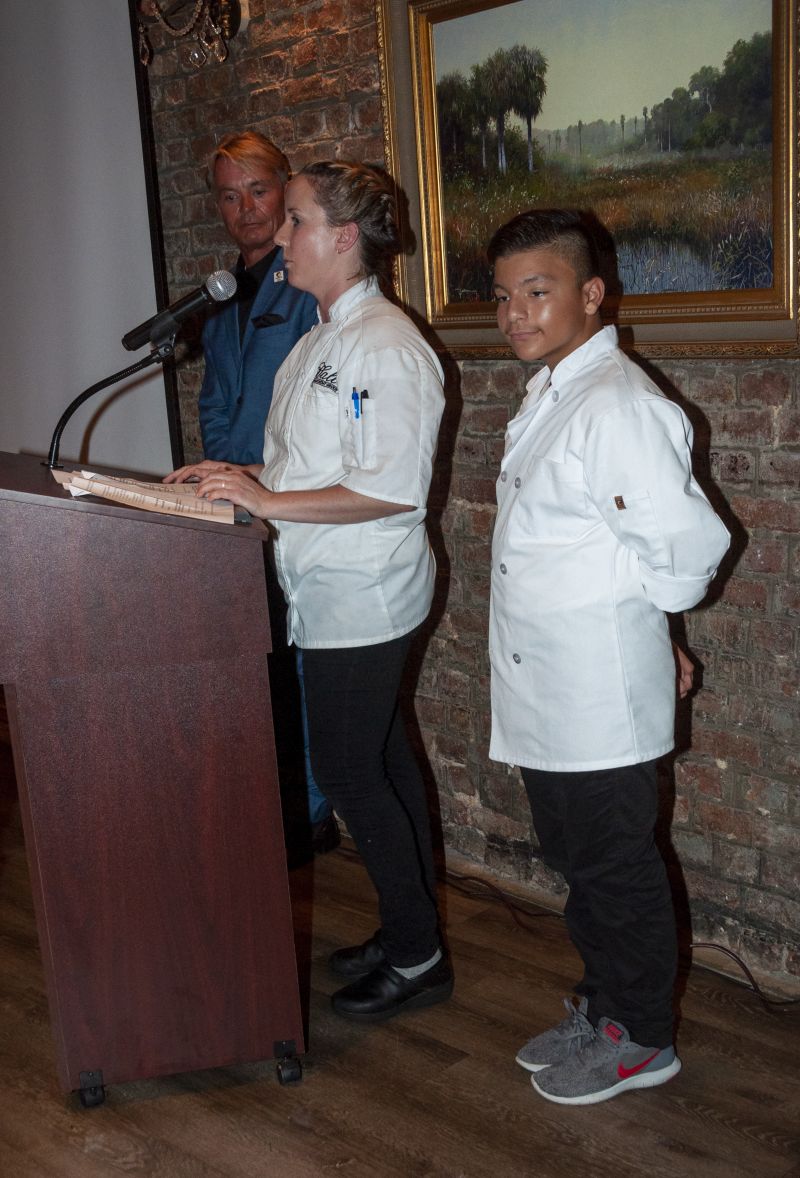Louis Yuhasz stands by as Big Chef Robyn Guisto of Halls Signature Events and Little Chef Abraham Aguilera present their dish to dinner guests.