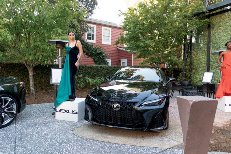 A model dressed by Menia Paige Couture poses near a Lexus RX.