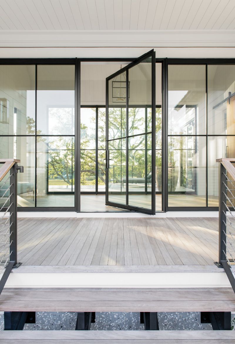 Steeling Beauty: At the top of the home’s floating outdoor staircase, the custom steel and glass pivot door made by Arcadia Custom Building Materials provides entry to the glass breezeway, its industrial feel softened by a serene view of oak trees and marsh just beyond.