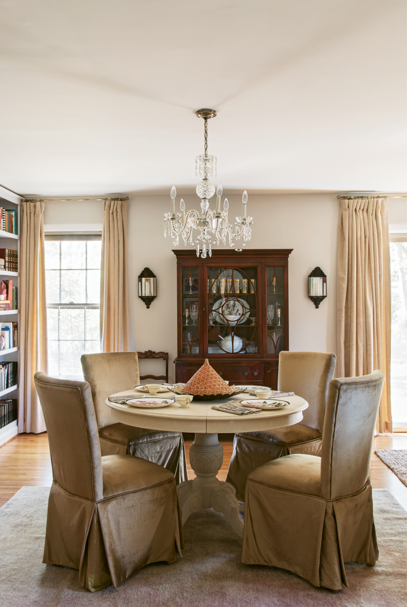 DINING IN STYLE: Velvety gold skirted dining chairs, a 1950s crystal chandelier, and mirrored sconces make the dining nook feel glamorous, while a handed-down hutch nods to tradition.