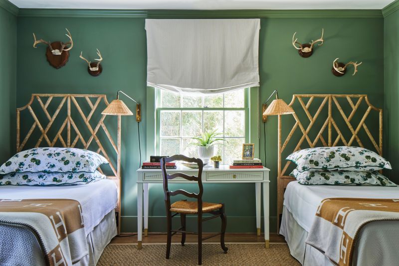 This guest room speaks toward nature, with mounted antlers, bamboo headboards, and sage green walls (Farrow &amp; Ball “Calke Green”). “We upgraded the standard pillows to king size, which makes sleeping solo in a twin bed the biggest treat,” says the designer.