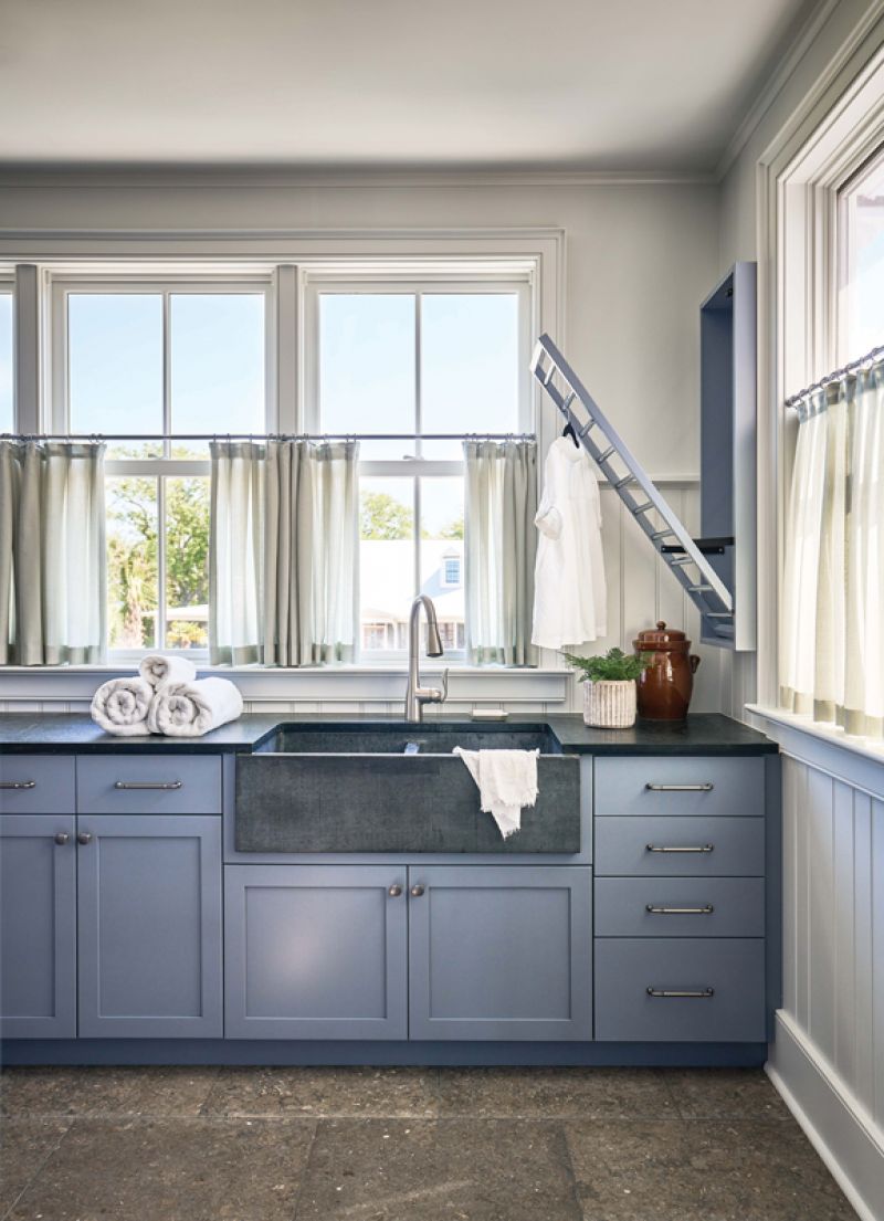 Chores with a View: Previously a guest bedroom, the laundry room offers expansive views over the marsh. A stone floor complements the soapstone sink repurposed from the original kitchen, and cabinets painted in Sherwin Williams “Storm Cloud” add a pop of color.