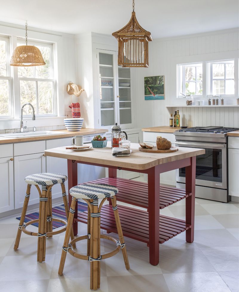 Gather ’round: Working around the original glass-fronted cabinets in the kitchen, Isbell added a butcher-block island to allow for flexible seating in the space. On the floor, a chessboard pattern painted by Suzanne Allen Studio continues the theme of painted wood flooring seen throughout the home.