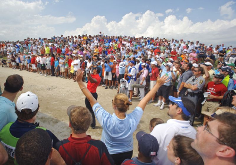 Tiger hitting out of the sand with a few spectators watching after an errant tee shot on number 10.