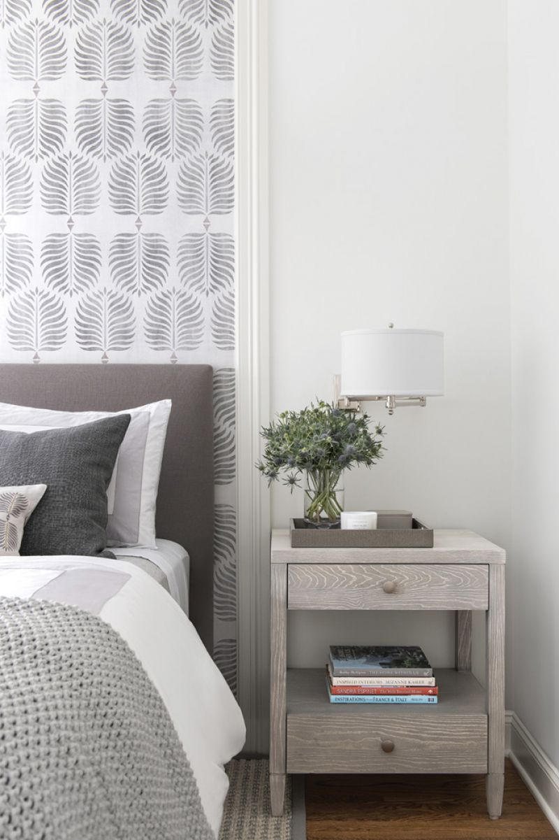 In the second guest room, the designer added panel modeling around a patterned wallpaper as a second headboard. The light gray of the paper is continued in the bedding and nightstand, which is topped by the Visual Comfort “Hudson Swing Arm” wall sconce in polished nickel from Circa Lighting.