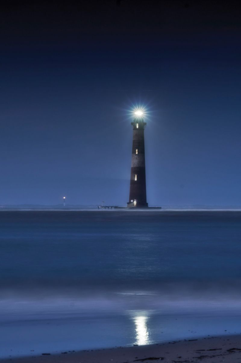 On September 18th, 2020, the Morris Island Lighthouse was lit in tribute to longtime local shrimper Wayne Magwood. The beam from the Sullivan’s Island Lighthouse (or Charleston Light) can be seen in the background. (photograph by Lou Vega)