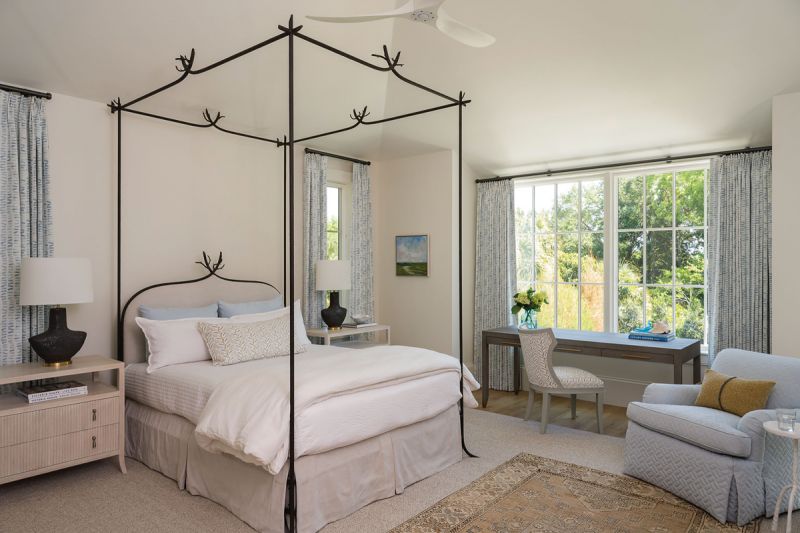 Into the Woods: Located on the main floor, the primary suite enjoys a lush view of the surrounding maritime forest, a fitting backdrop for the “Twig” iron bed by Formations that was originally in the couple’s mountain home. Designers Means &amp; Carney softened the look with floral fabrics, including pretty blue drapes by Savannah Hayes.