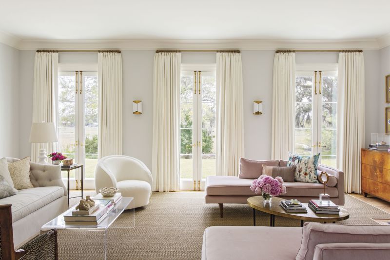 La Vie En Rose: Natural light spills into the living room through French doors, framed by custom drapes in a Joseph Noble fabric. The soothing palette, anchored by walls in Farrow &amp; Ball “Blackened,” is complemented by pops of pink from two West Elm chaises re-covered in Kravat velvet.