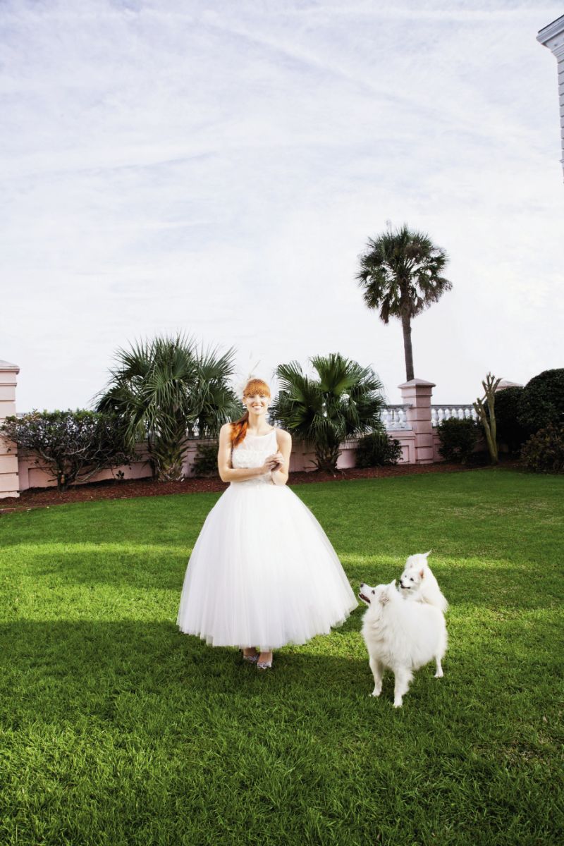 PUPPY LOVE:  Steven Birnbaum’s “Daisy” tulle tea-length gown with sheer bateau neckline and floral accents from White. Cage veil headband with feather accents  from Out of Hand. Nina’s d’Orsay heels from LulaKate.