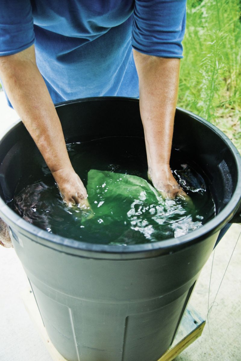 After preparing her dye with indigo extract, Donna folds in damp clean linen in an accordion fashion and continually swirls the fabric for about a minute to prevent air bubbles as it turns a chartreuse green.