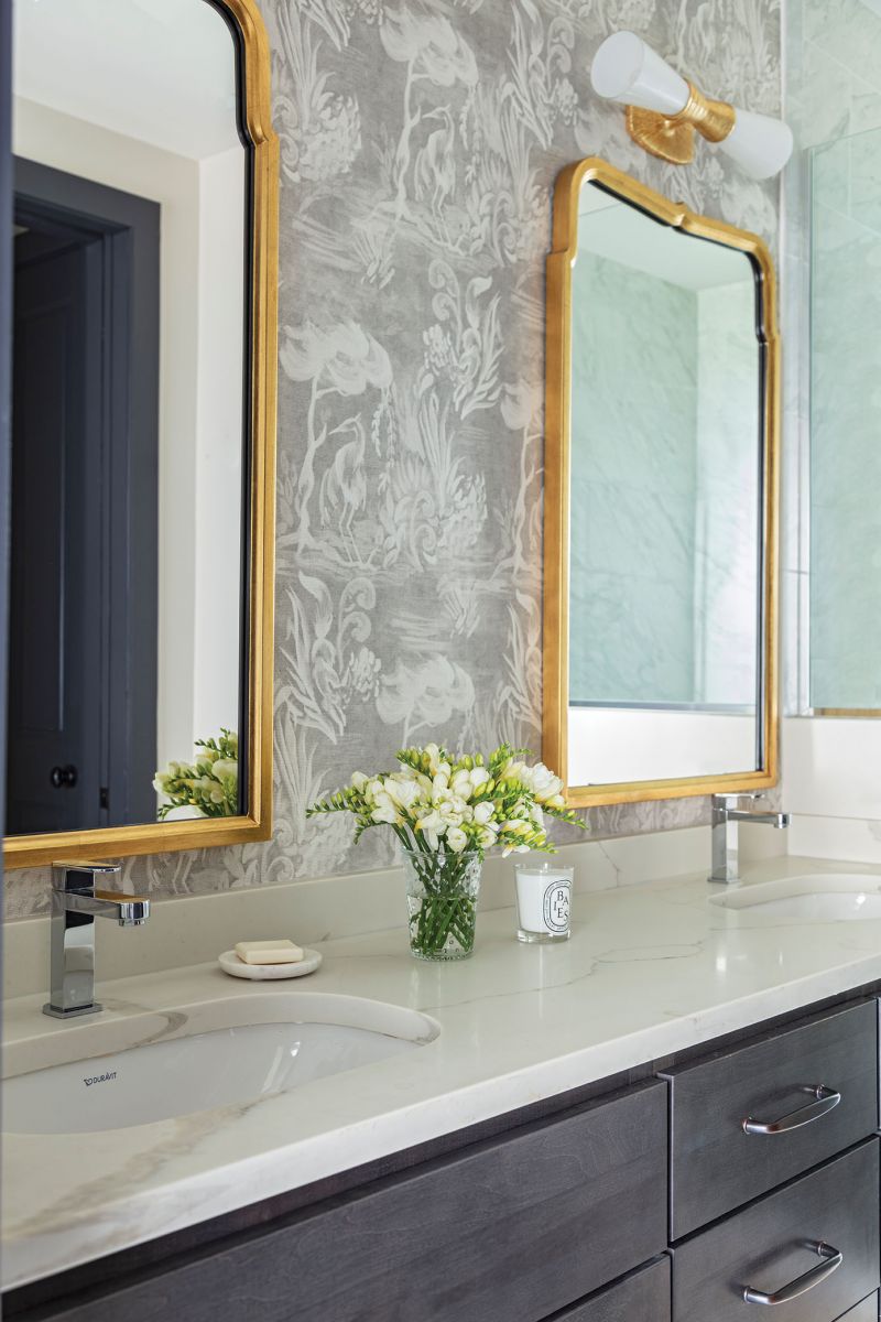 The wallpaper continues into the bathroom, where two brass-accented vanity mirrors from Mirror Home are illuminated by Visual Comfort wall sconces.