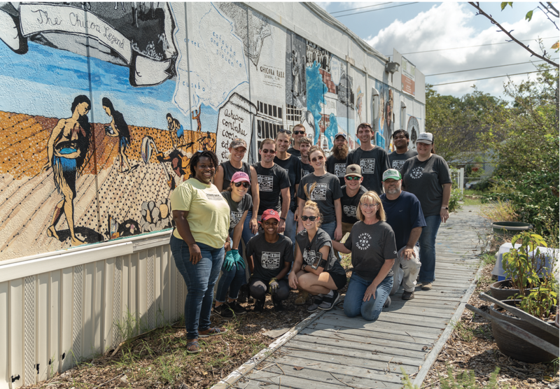 All Hands on Deck: The farm’s core team gets lots of help from volunteers, such as these employees from Stantec, pictured with Jenkins next to the farm store. The mural, which special projects manager Anik Hall researched, organized, and painted, depicts 500 years of the Chicora-Cherokee neighborhood’s history.