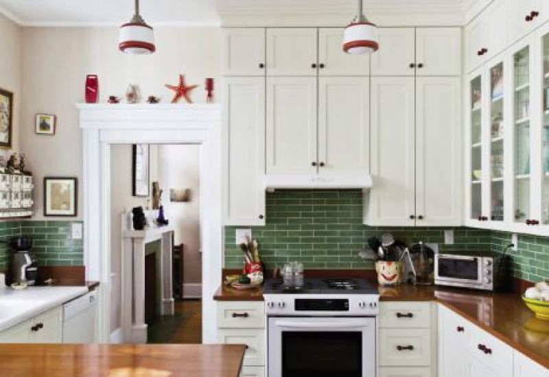 Emerald green ceramic tiles, ruby red cabinet pulls, and schoolhouse-style pendant lighting headline the recently renovated kitchen